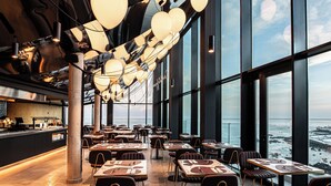 Un restaurant avec une grande table centrale, de grandes fenêtres et des luminaires sphériques suspendus.