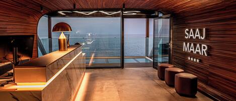 Un interior moderno con techo de madera, mostrador de recepción y pared de vidrio con vistas al mar.