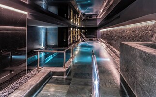 Un moderno espacio de spa con una fuente central, paredes de piedra y barandillas metálicas.