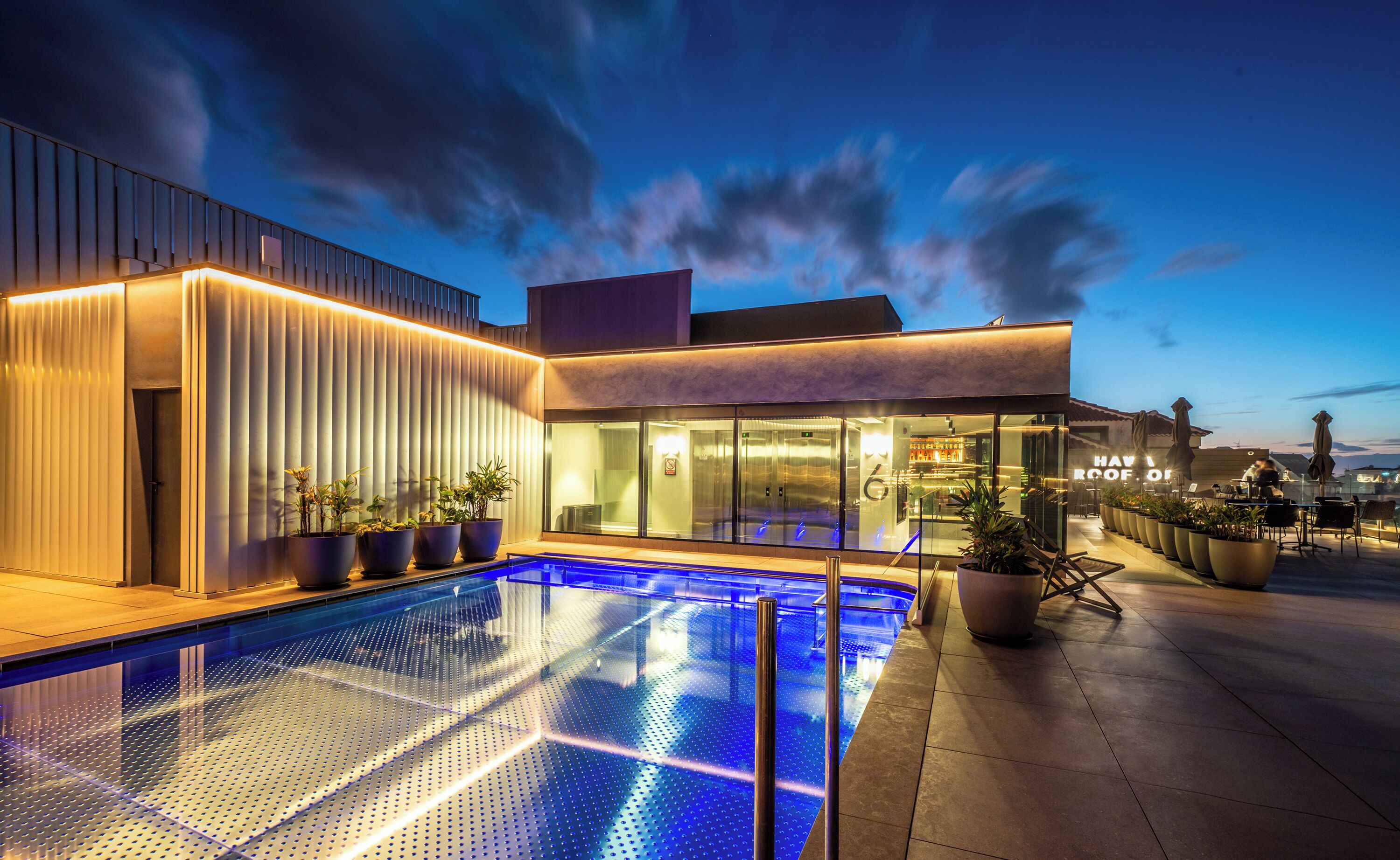 A modern hotel with a swimming pool, outdoor seating, and a bar area.