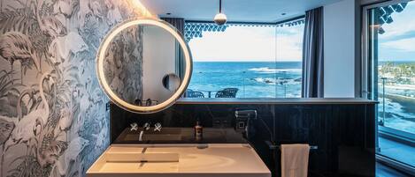 A modern bathroom with a large mirror, a sink, and a view of the ocean.