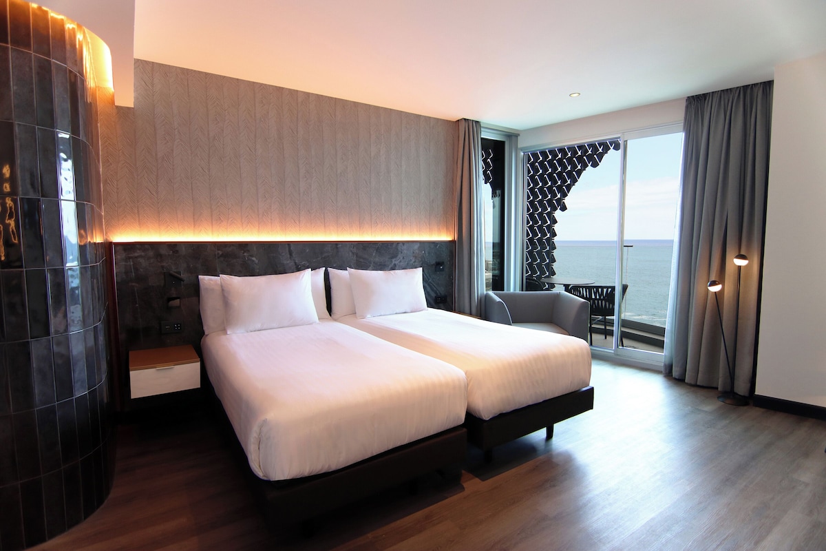 A hotel room with a large bed, a desk, and a view of the sea.