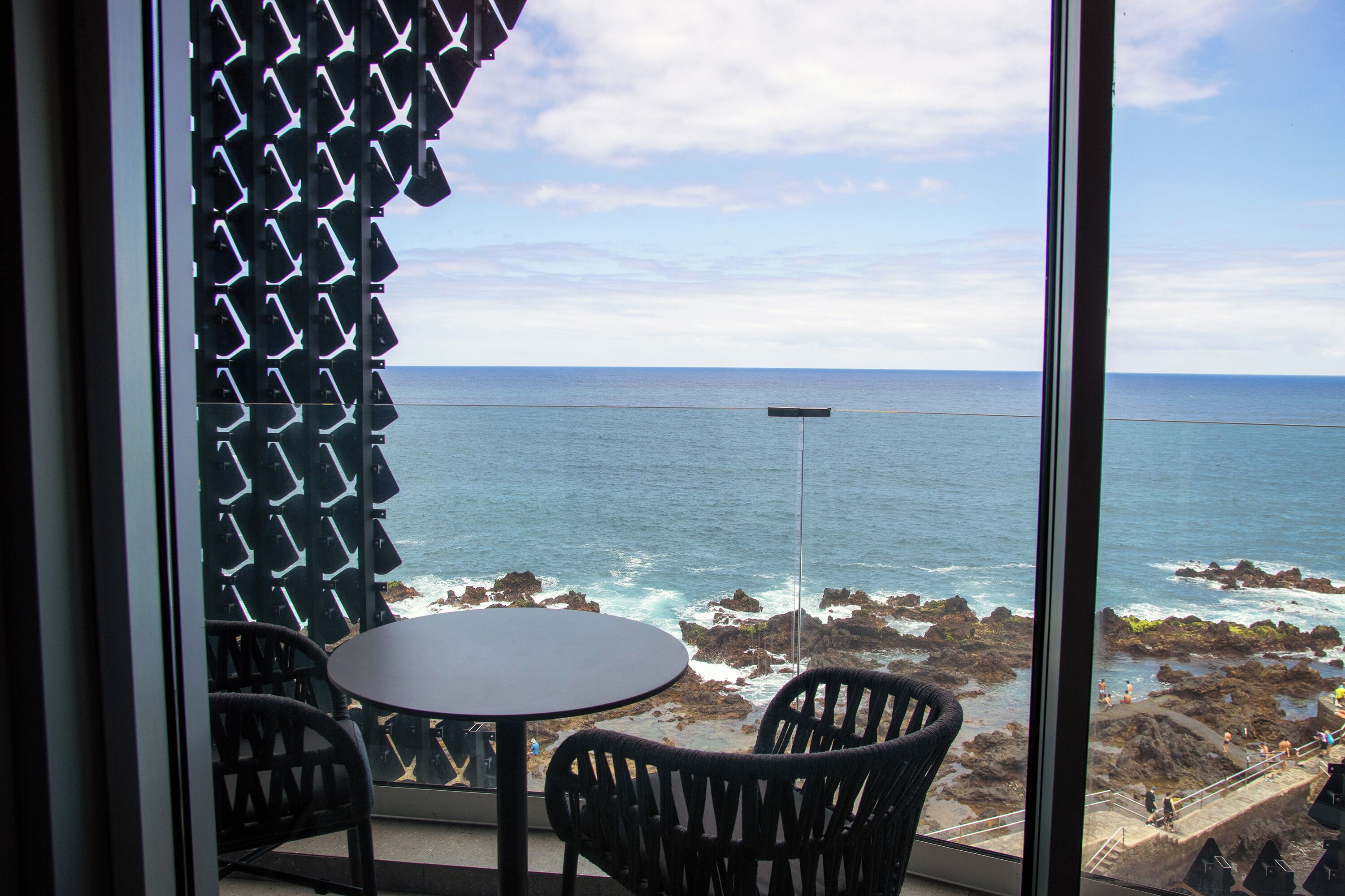 Un balcón con mesa y sillas, con vista a un litoral rocoso y el mar.