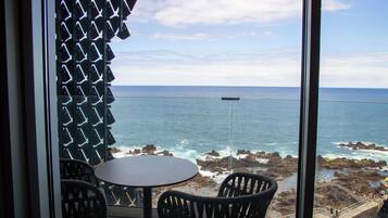Un balcón con mesa y sillas, con vista a un litoral rocoso y el mar.