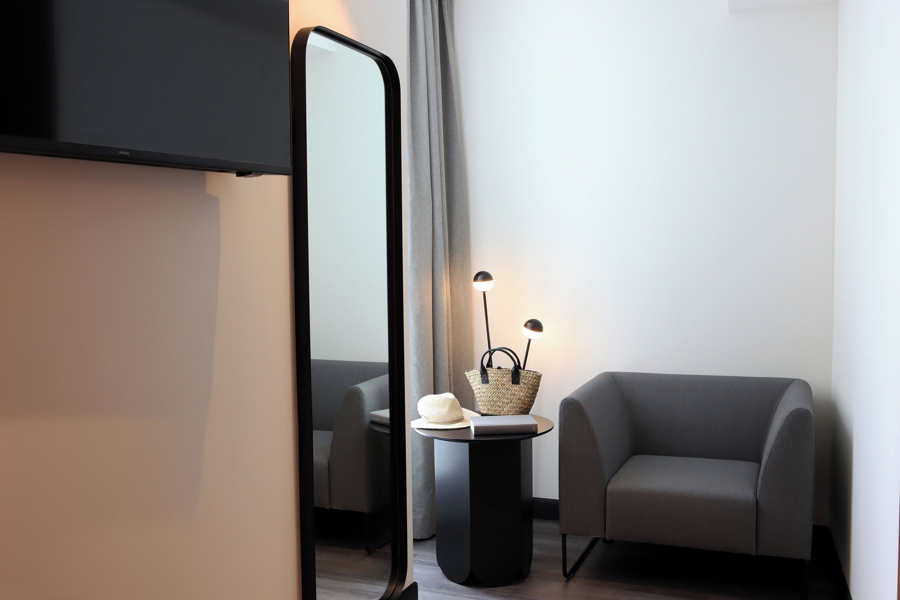Ein modernes Zimmer mit einer Couch, einem kleinen Tisch mit einer Lampe und einem Spiegel.