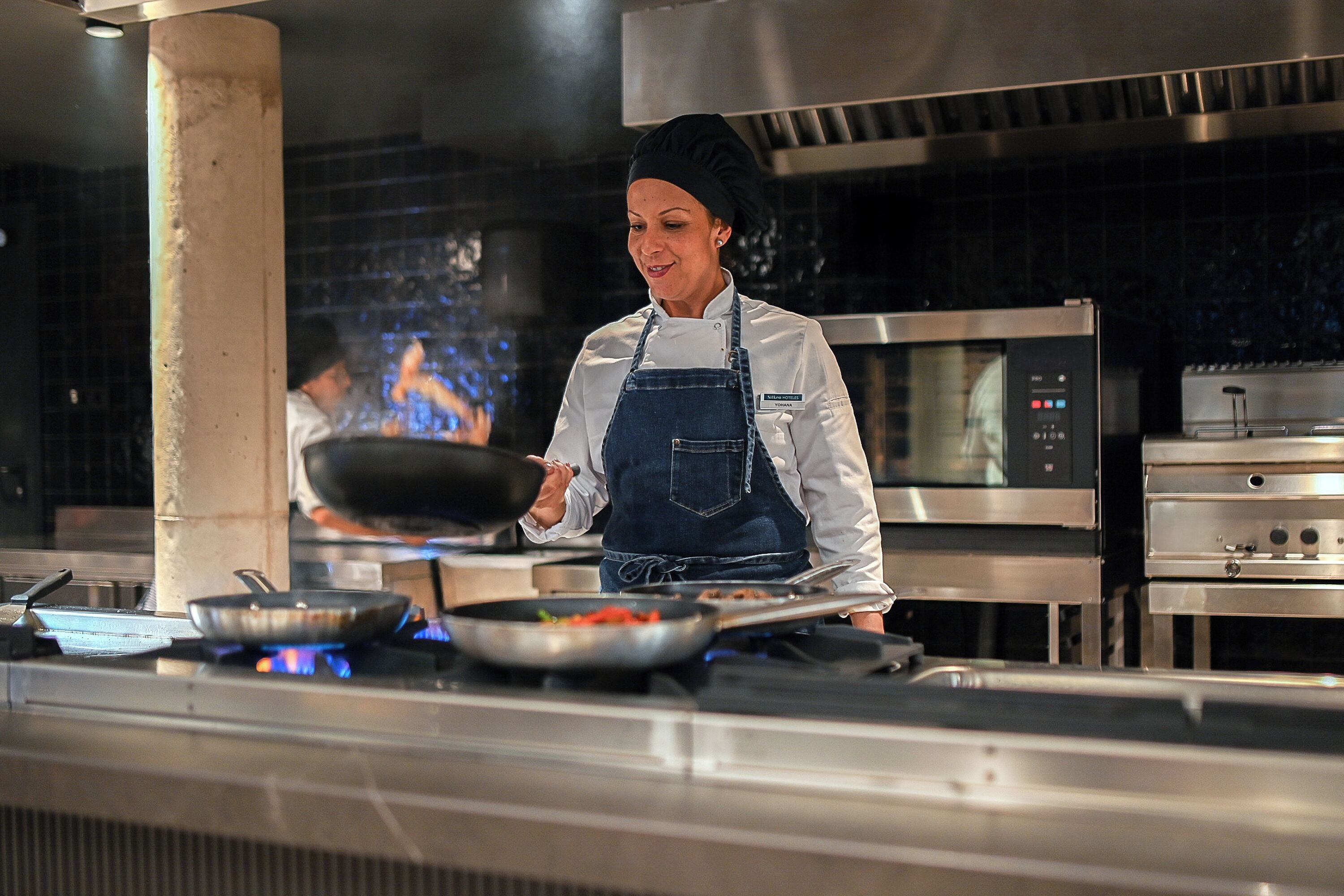 En kock i ett professionellt kök med rostfria köksmaskiner, inklusive en spis och en mikrovågsugn.