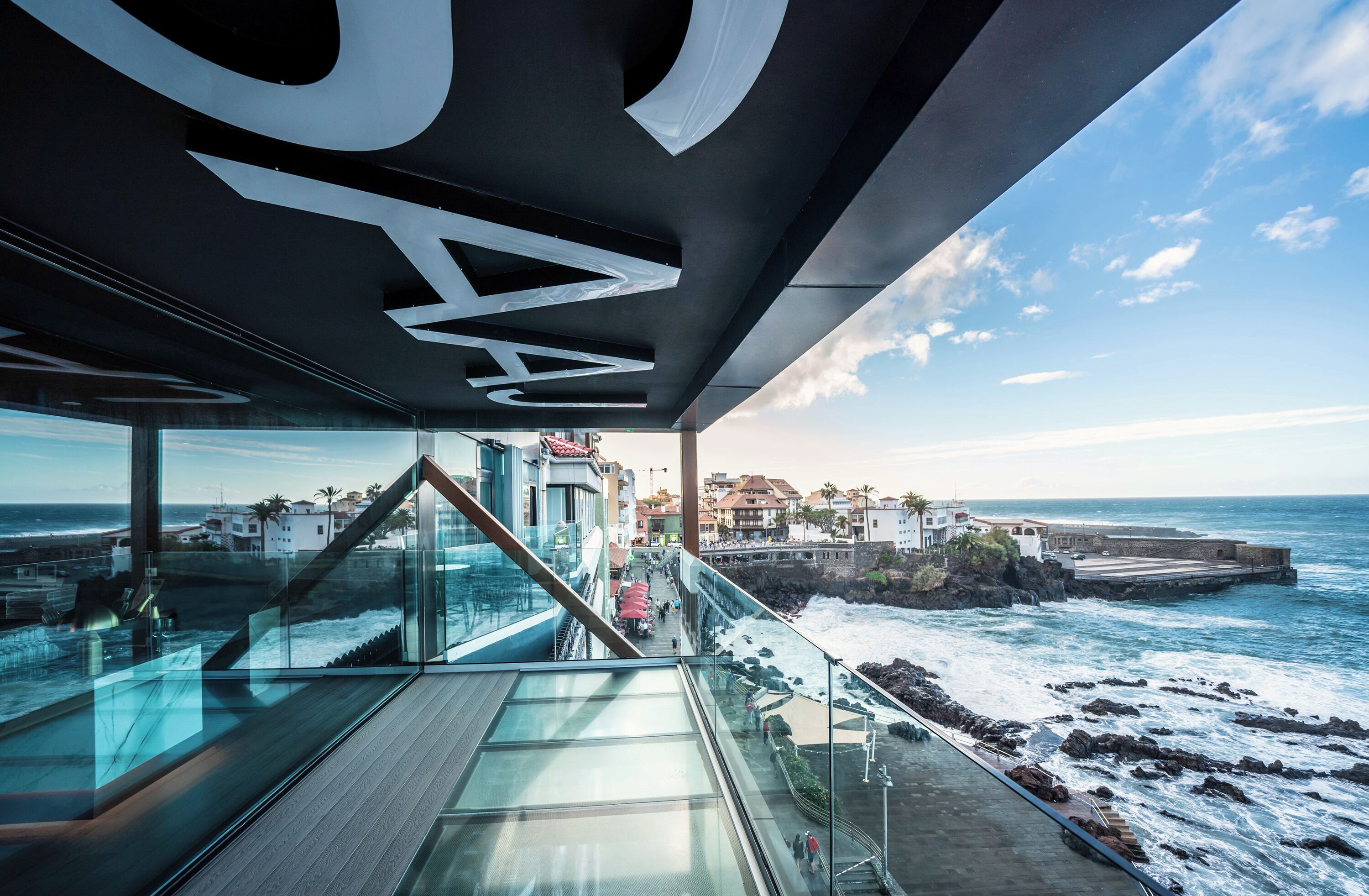 A modern building with a glass facade overlooking a coastal area.