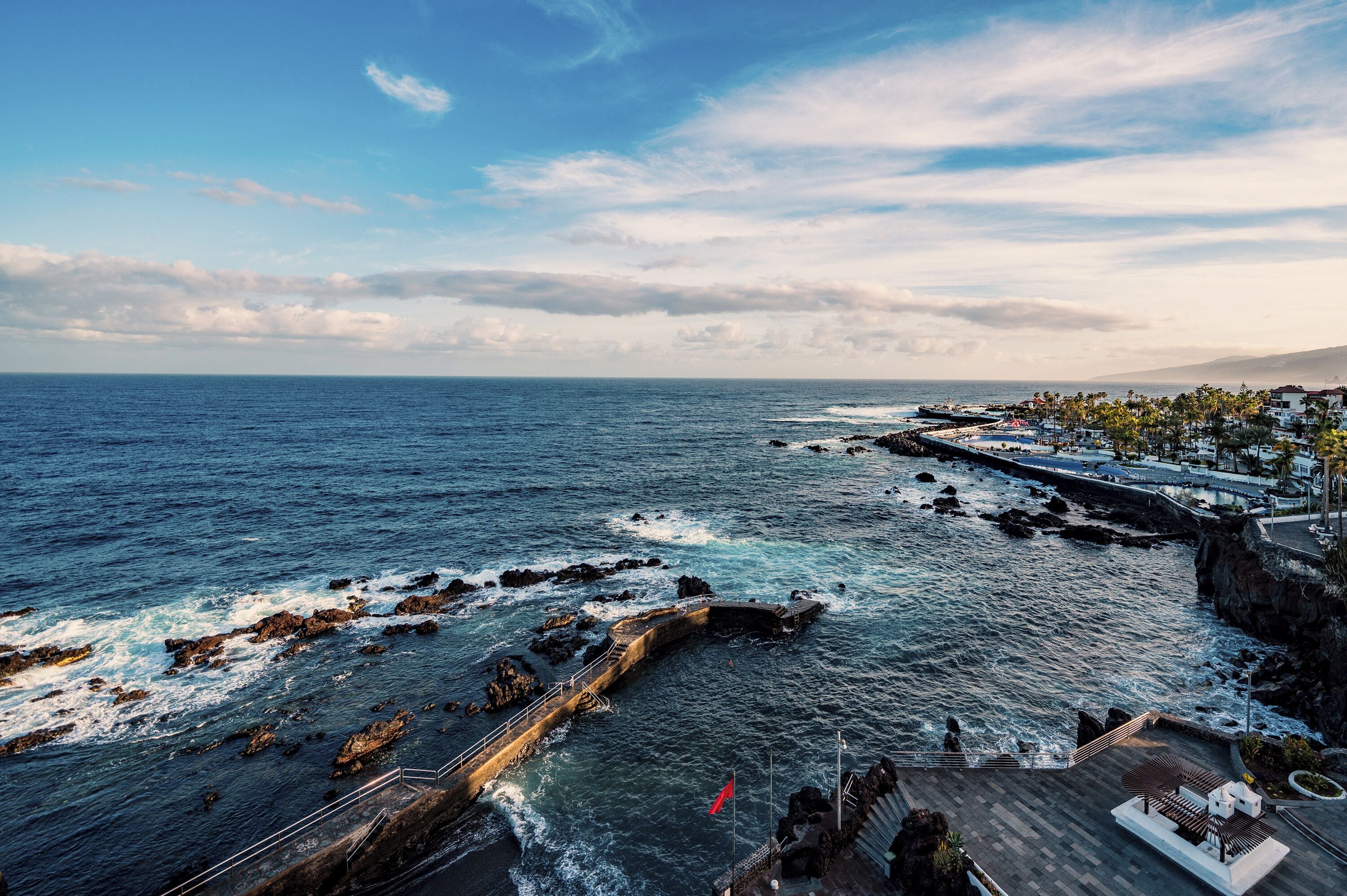 Une vue sur la côte, avec un rivage rocheux, une promenade agrémentée de bancs et un ciel dégagé.