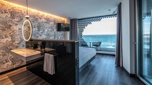 Une chambre d’hôtel moderne dotée d’un grand lit, d’une salle de bain avec un meuble-lavabo et d’un balcon offrant une vue sur l’océan.