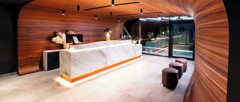 Un área de recepción moderna con una pared curva de madera, un mostrador de mármol y una zona de estar con taburetes acolchados.