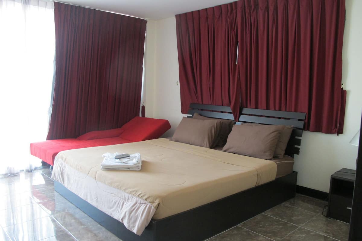 Quarto de hotel com uma cama grande, cortinas vermelhas e um sofá vermelho.