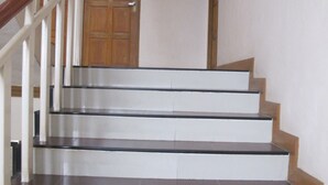 A staircase with white steps and dark treads, wooden handrails, and a wooden door at the top. - Rouge Service Apartments (Pattaya)