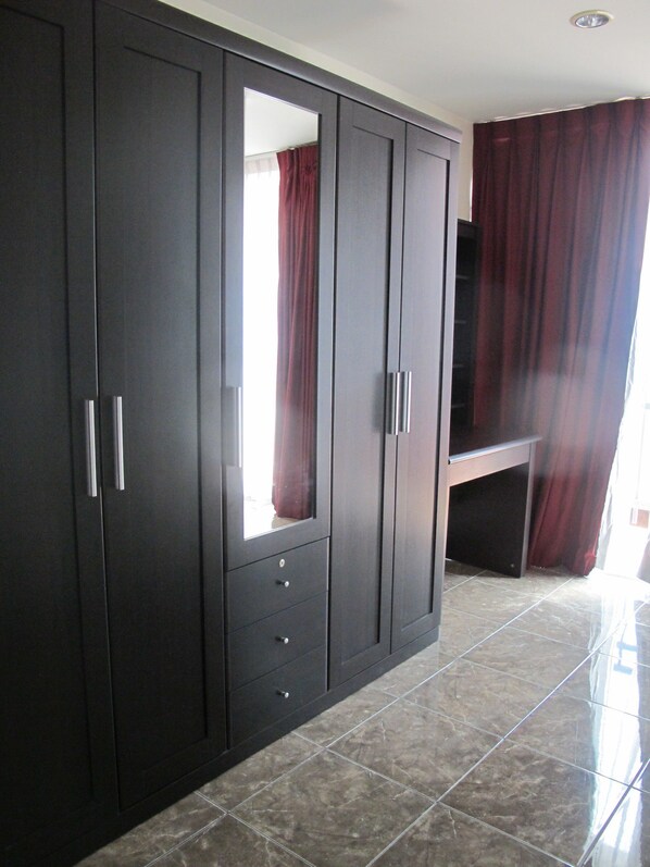A large wardrobe with mirrored doors and a bench, in a room with tiled flooring.