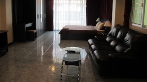A modern hotel room with a bed, a leather sofa, a glass coffee table, and a TV. - Rouge Service Apartments (Pattaya)