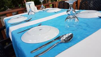 Mesa lista para comer al aire libre, con mantel azul, platos blancos y vasos de vidrio transparente.