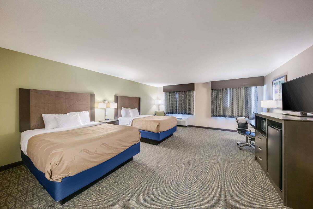 Une chambre d’hôtel avec deux lits, un bureau, une télévision et une fenêtre avec des rideaux.