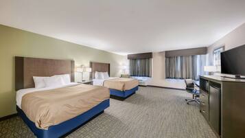 A hotel room with two beds, a desk, a TV, and a window with curtains.