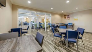 A spacious dining area with multiple tables and chairs, a kitchen in the background, and a large window providing natural light. - Quality Inn & Suites Ardmore (Ardmore)