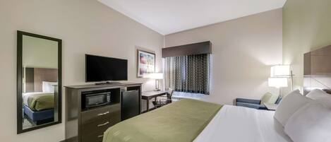 A hotel room with a bed, a desk with a computer, a television, a microwave, and a mirror.