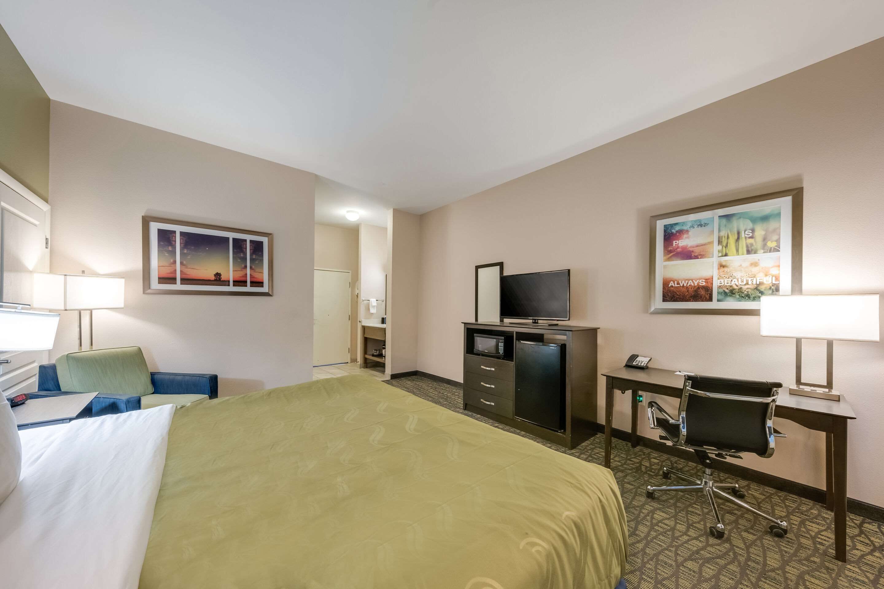 A hotel room with a bed, desk, chair, television, and a small refrigerator.