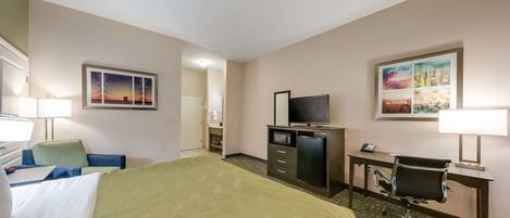 A hotel room with a bed, desk, chair, television, and a small refrigerator.