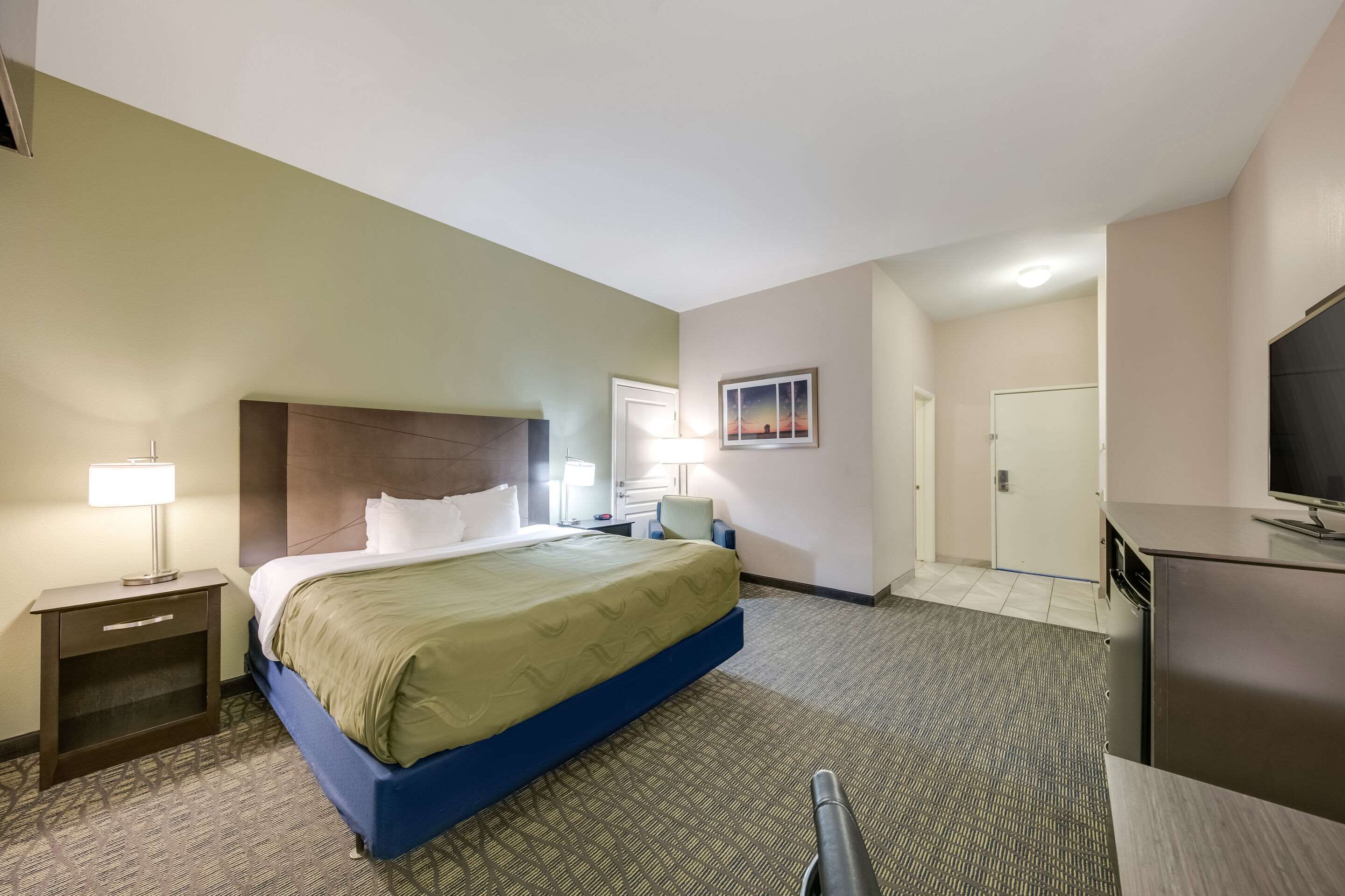 A hotel room with a bed, nightstands, a desk, a television, and a door.