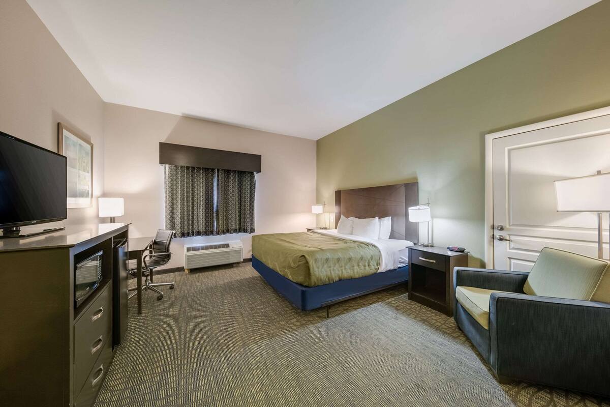Une chambre d’hôtel avec un lit, un bureau, une chaise, une télévision et une fenêtre avec des rideaux.