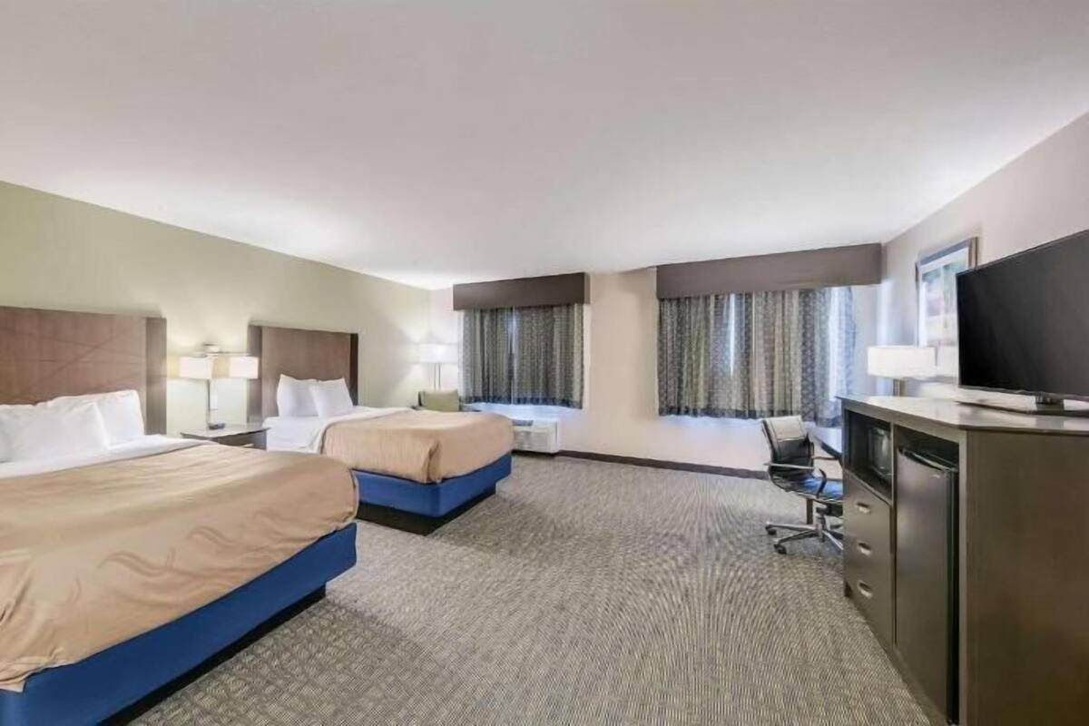 Une chambre d’hôtel avec deux lits, un bureau, une télévision et une fenêtre avec des rideaux.