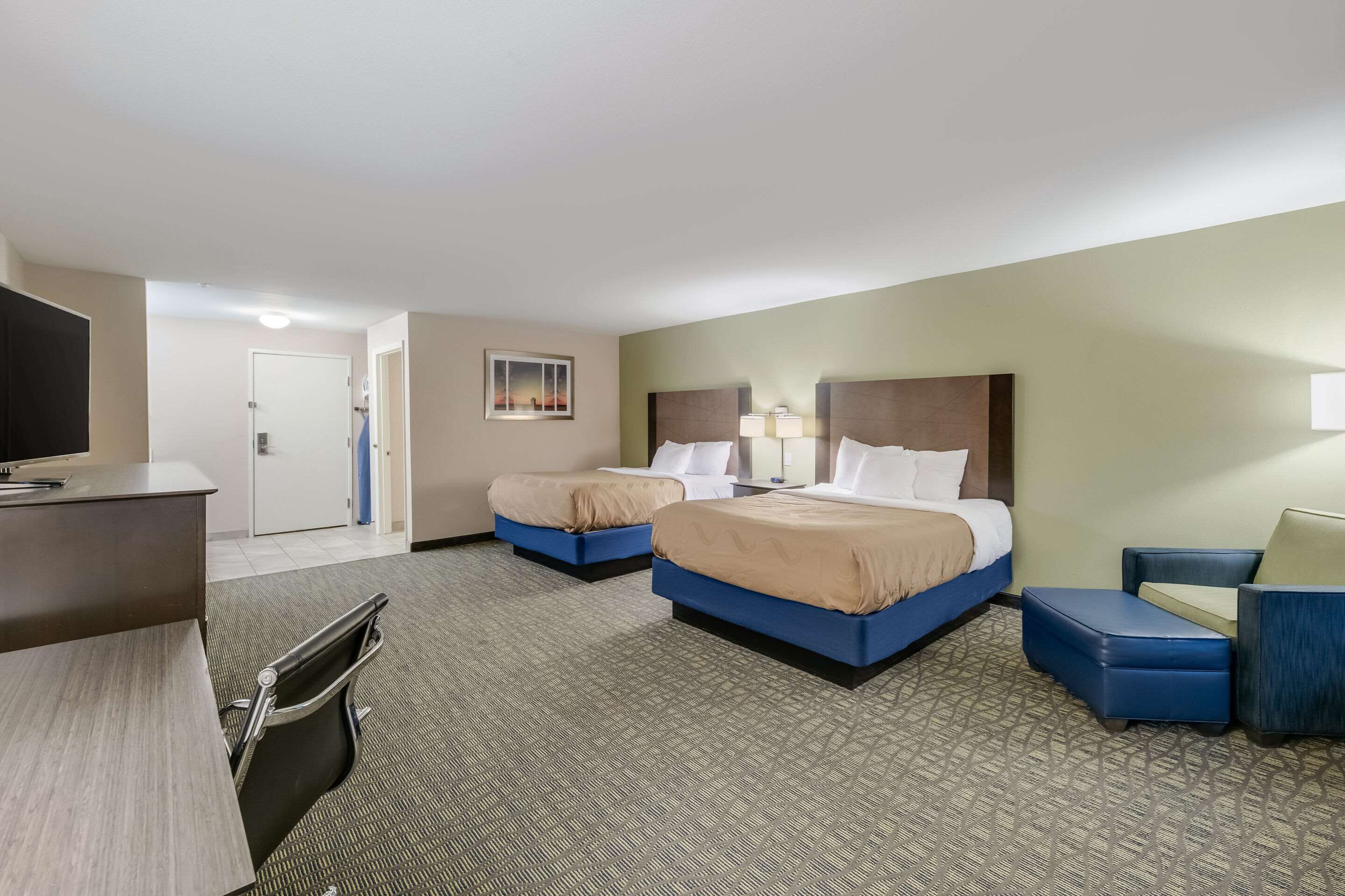 Quarto de hotel com duas camas, uma escrivaninha, uma cadeira e uma televisão.
