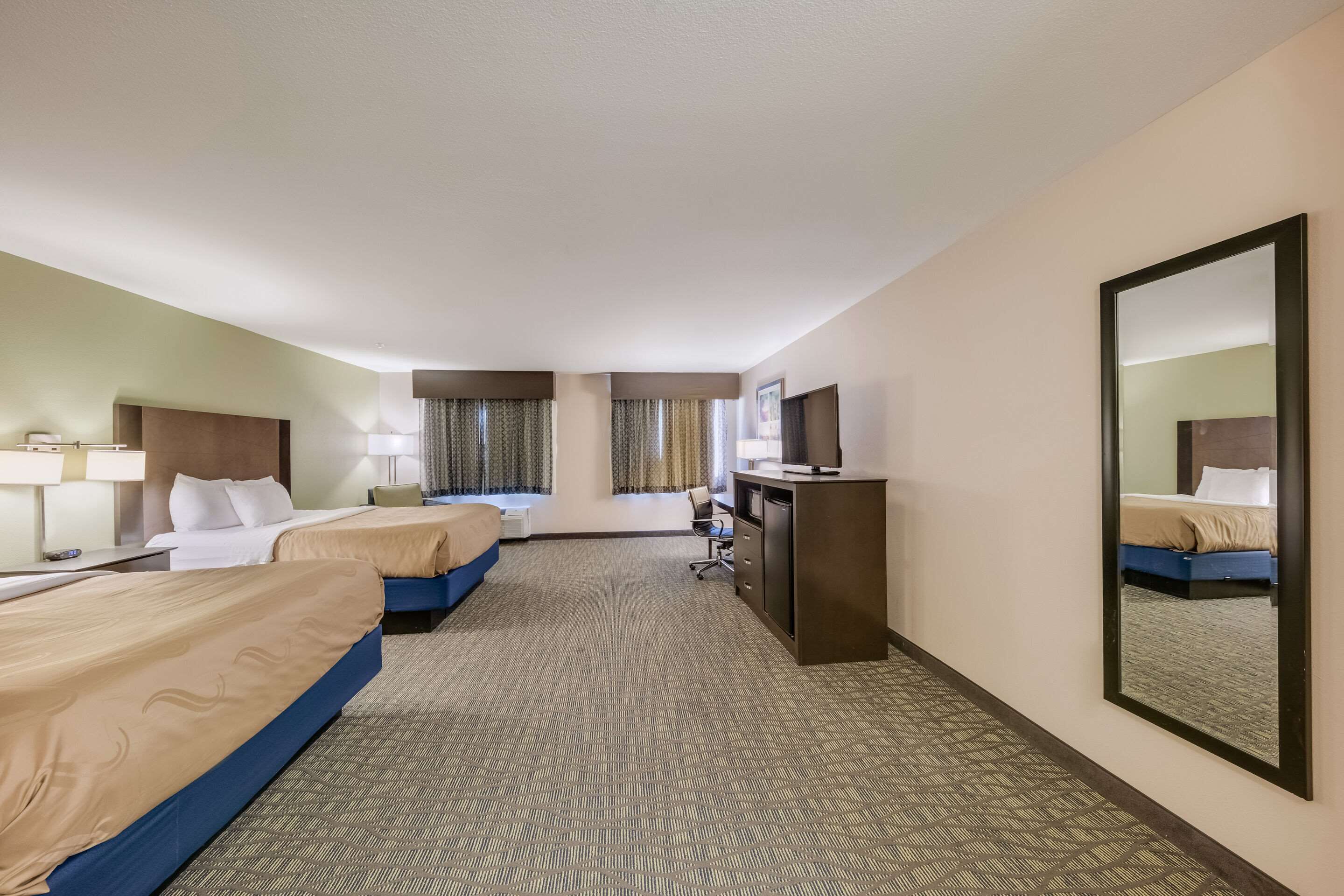 A hotel room with two beds, a desk, a chair, a television, and a large mirror.