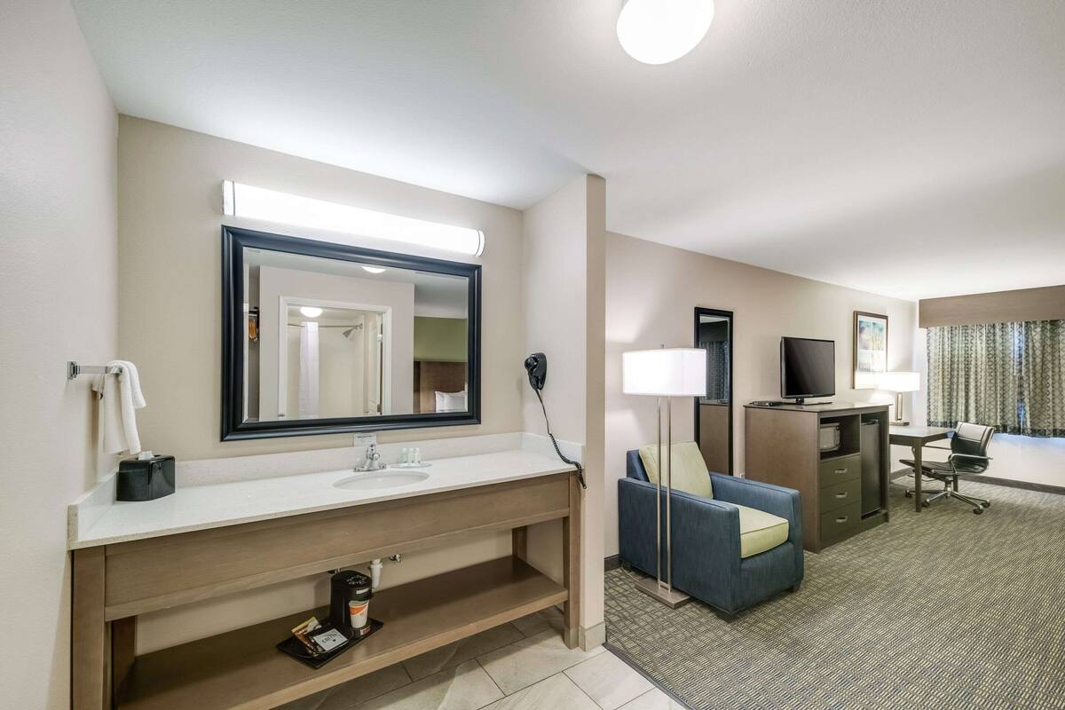 Une chambre d’hôtel équipée d’un grand miroir, d’un lavabo, d’un canapé, d’un bureau avec un ordinateur et d’une télévision.