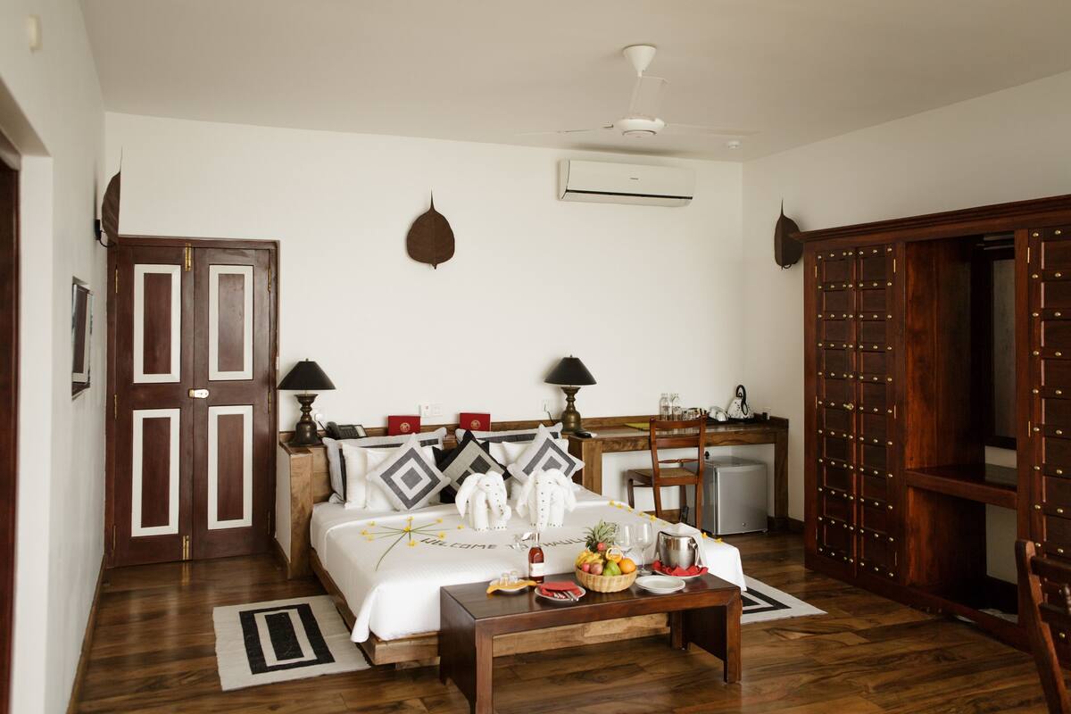 A hotel room with a bed, bedside lamps, a desk with a fruit basket, a minibar, and a wardrobe.