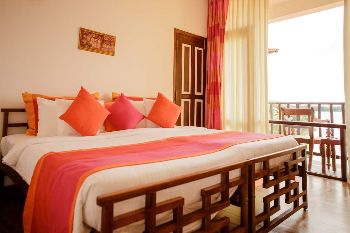 A neatly made bed with a wooden headboard, a balcony with a table and chairs, and a door with a curtain.