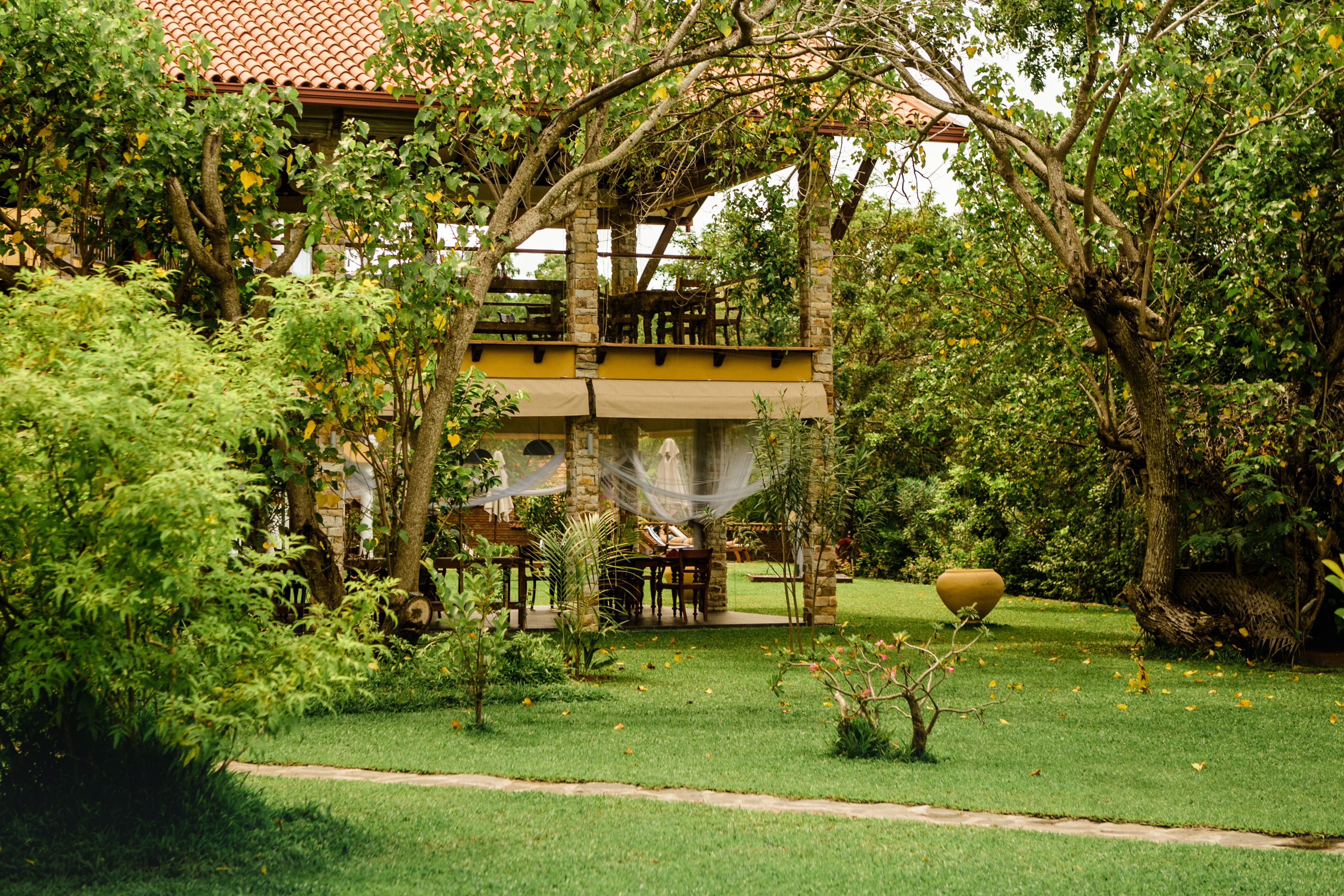 A two-story building with a red-tiled roof, surrounded by lush greenery and trees.