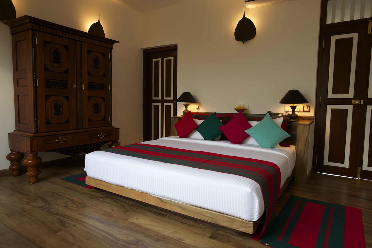A neatly made bed with a striped bedspread, a wooden wardrobe, and two wall-mounted lamps.