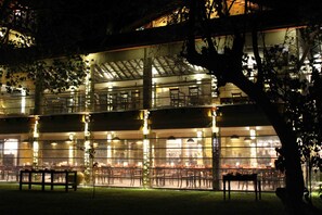 Un edificio de varios pisos con fachada de vidrio, zona de estar al aire libre y un banco.