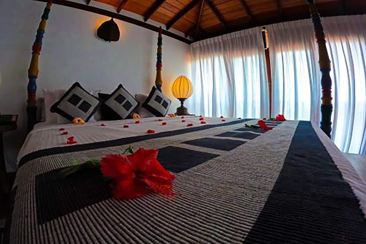 A four-poster bed with a striped bedspread, decorative pillows, and a single red flower on the bed.
