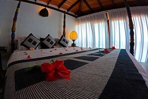 Una cama con dosel, con colcha a rayas, almohadas decorativas y una sola flor roja sobre la cama.
