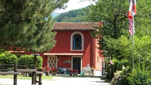 A red building with a tiled roof, a stone statue in front, and a flagpole with a flag. - Podere Campofossato (Pistoia)