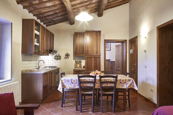 A kitchen with wooden cabinets, a dining table with chairs, and a tiled floor.
