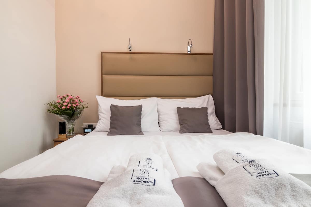 A hotel room with a large bed, two pillows, a nightstand with a vase of flowers, and a headboard.