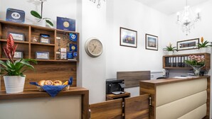 A reception area with a wooden reception desk, a clock, framed pictures, and a plant. - G12 Aparthotel (Kraków)