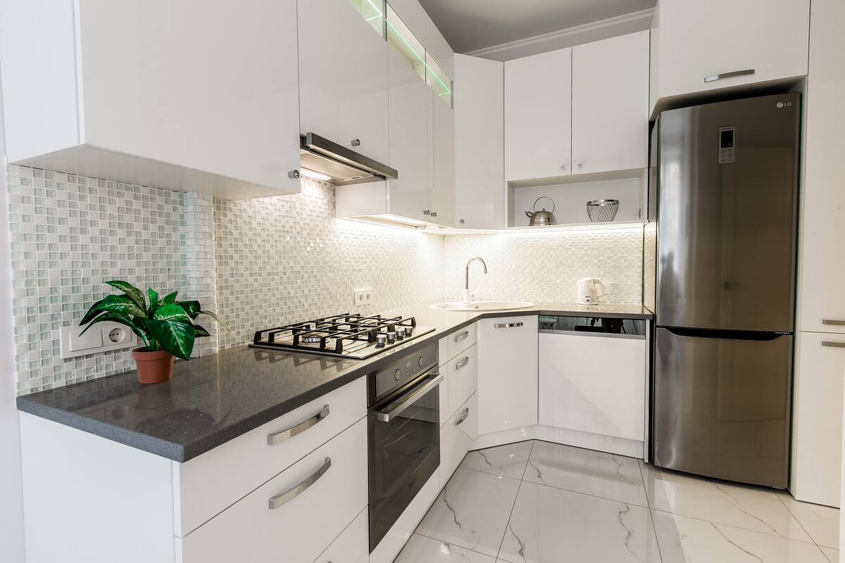 A modern kitchen with white cabinets, a stainless steel refrigerator, a gas stove, and a tiled backsplash.