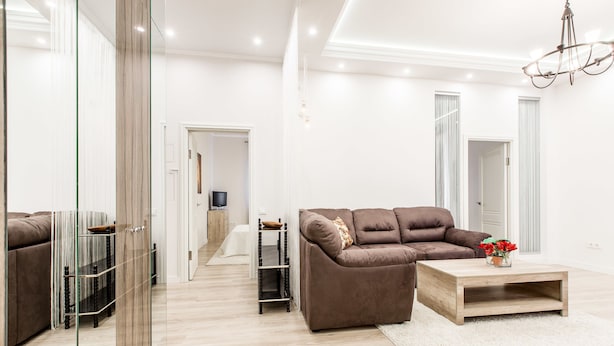 Uma sala de estar moderna com um sofá marrom, uma mesa de centro de madeira e um separador de vidro.