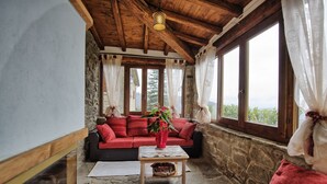 A cozy room with a stone wall, a red sofa, a wooden ceiling, and large windows. - Villa Margherita Tre (Cortona)