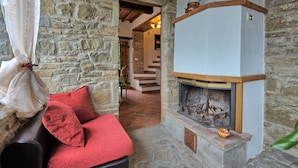 A stone-walled room with a fireplace, a bench with red cushions, and a staircase leading to another area. - Villa Margherita Tre (Cortona)