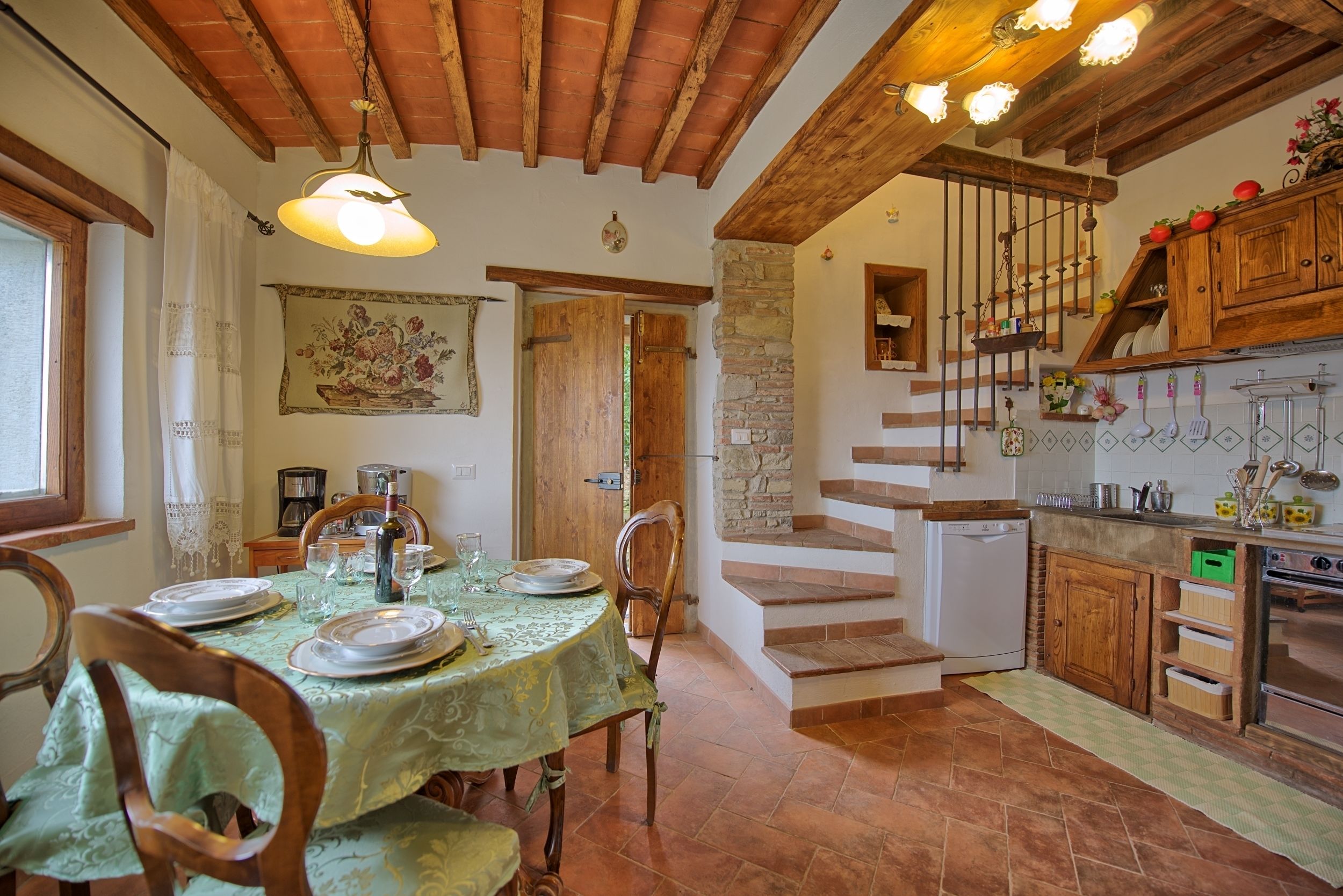 A rustic kitchen with a dining area, wooden beams, stone walls, and a staircase.