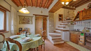 A rustic kitchen with a dining area, wooden beams, stone walls, and a staircase. - Villa Margherita Tre (Cortona)