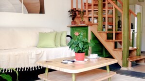 A modern living room with a wooden staircase, a white sofa, a coffee table, and a potted plant. - Pia Aparts (Kemer)