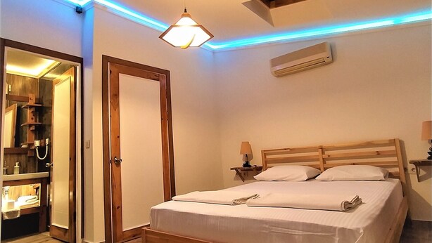 A bedroom with a wooden bed, a nightstand, a wall-mounted air conditioner, and a ceiling light fixture. - Pia Aparts (Kemer)